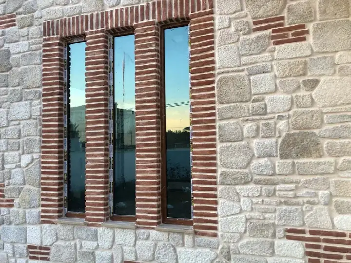 Açık renk kesme taş cephede kırmızı tuğla çerçeveli dar pencereler