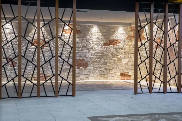 Gizli aydınlatmalı açık renk taş duvarın önünde metal desenli paravanlar