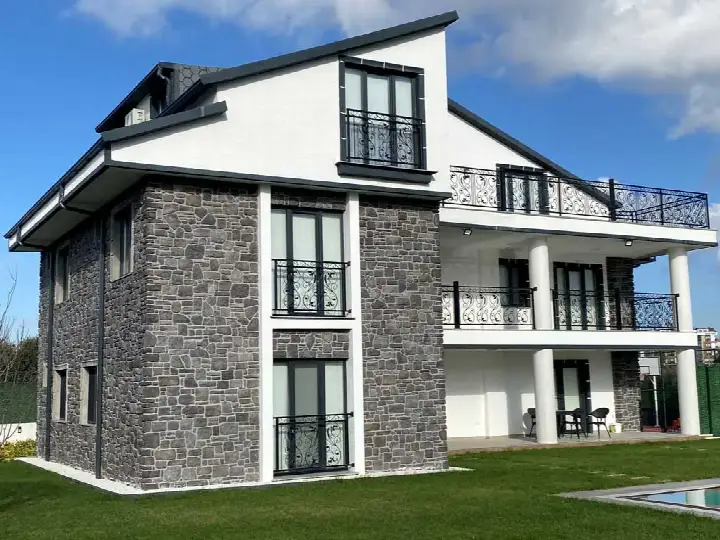 Balkonlu beyaz villanın iki yanındaki gri taş kaplı kütleler