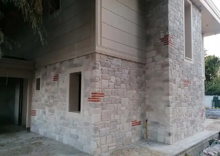 Bina köşesinde açık renk taş kaplama arasında dağınık kırmızı tuğla izleri
