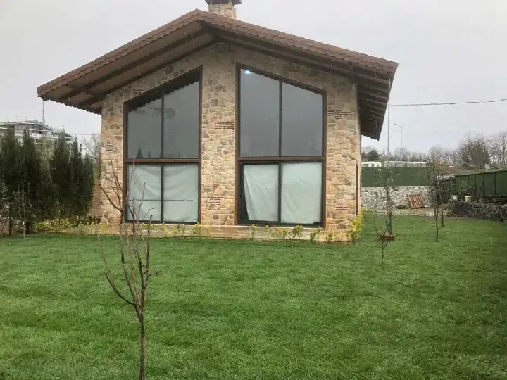 Büyük cam cepheli, sarı-kahve taş kaplı tek katlı ev