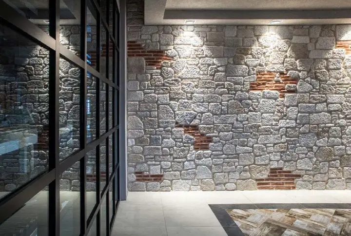 Siyah cam doğrama yanında tuğla serpiştirilmiş açık renk taş duvar
