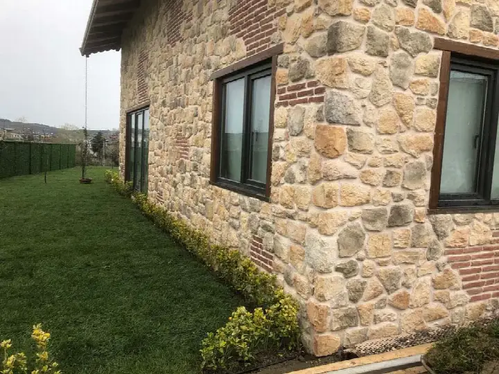 Çimenli bahçede sarı-kahve tonlu taş kaplı tek katlı ev