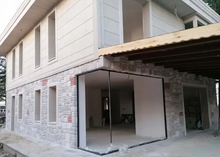 Geniş cam açıklıklı yapının taş kaplı cephesi ve saçak altı
