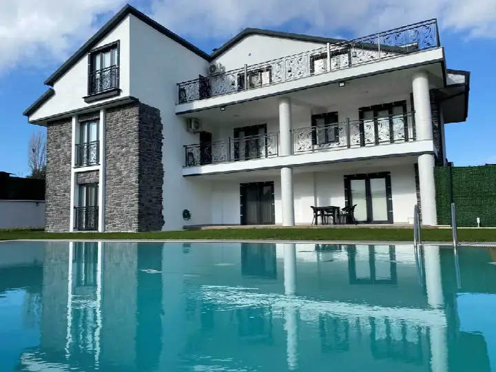 Havuz kenarındaki beyaz villanın taş kaplı yüzeyi ve sudaki yansıması