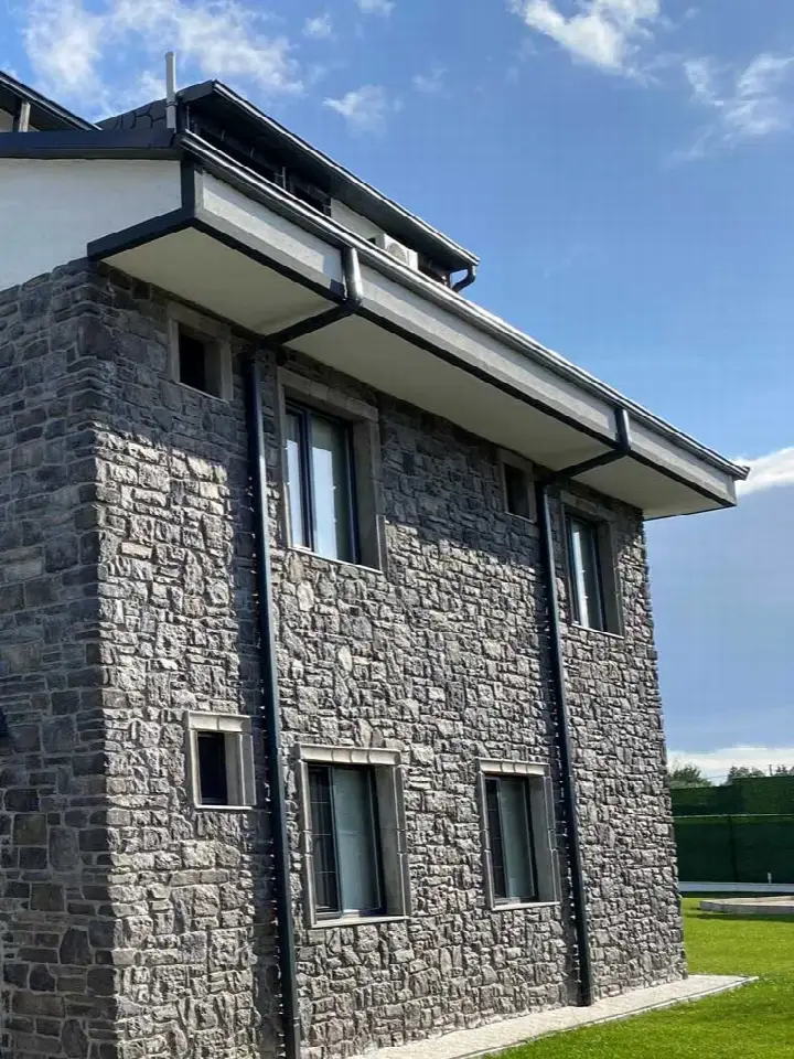 Koyu gri taş kaplı yüksek villa cephesi, alttan bakış