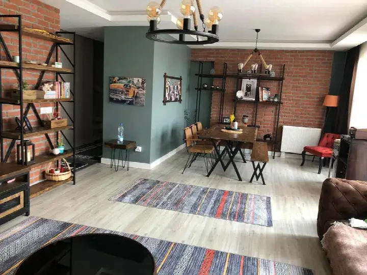 Mavi boyalı duvarın yanında kırmızı tuğla TV duvarı ve yemek alanı