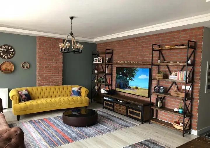 Sarı koltuklu salonda TV ünitesi arkasında kırmızı tuğla duvar ve metal raflar