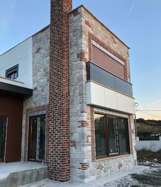 Kırmızı tuğla kaplı baca kütlesi ve açık renk taş cepheli ev