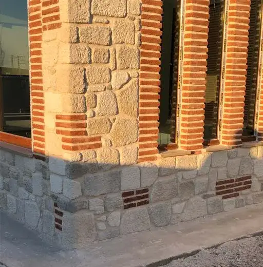 Pencere kenarında kırmızı tuğla söve ile açık renk taş duvarın birleşimi